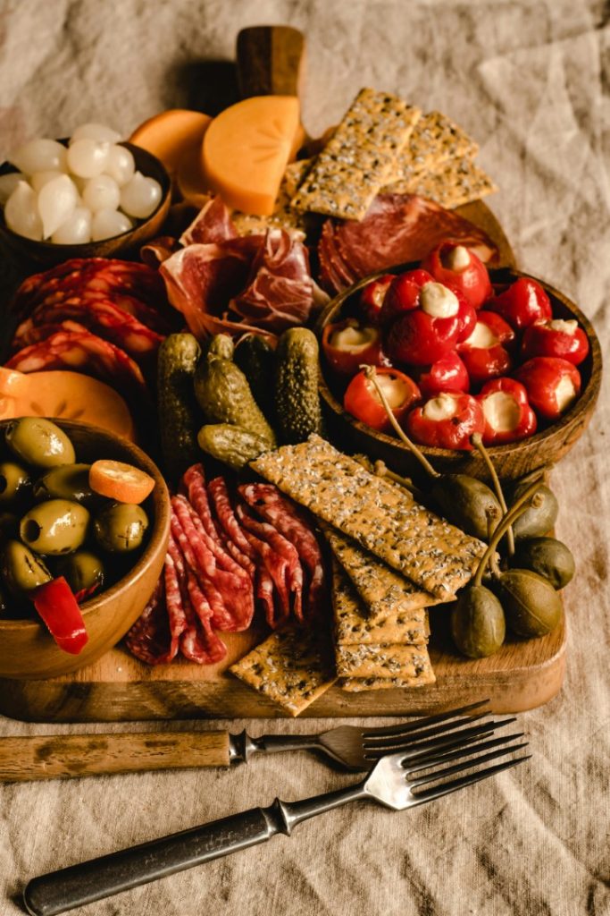 A rustic and appetizing charcuterie board filled with an assortment of cured meats, cheeses, olives, pickles, and crackers is arranged elegantly for a delightful snacking experience. Explore images