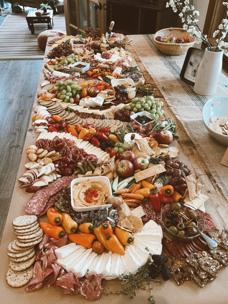 An expansive and beautifully arranged charcuterie board brimming with an assortment of cheeses, essentials like cured meats, fresh fruits, nuts, and crackers, set upon a long wooden table, beckoning guests