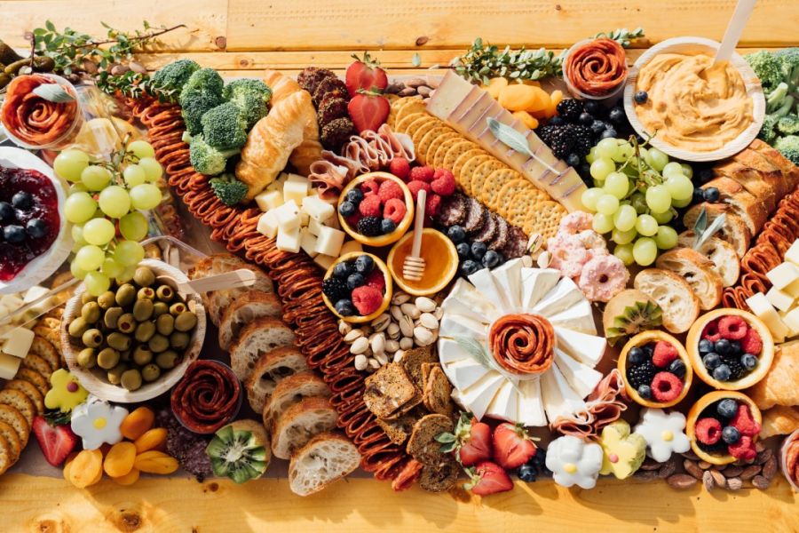 A lavish charcuterie board brimming with an assortment of essentials such as cured meats, cheeses, fruits, nuts, and dips, artfully arranged for a feast of flavors and colors.