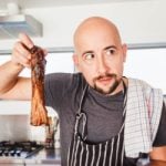 A pensive chef in a striped apron holding up a grilled rib, seeming to contemplate the quality of his barbecue masterpiece.