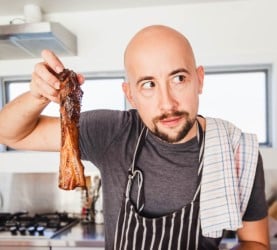 A pensive chef in a striped apron holding up a grilled rib, seeming to contemplate the quality of his barbecue masterpiece.