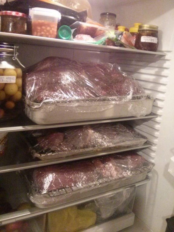 A fridge stocked with large cuts of age venison wrapped in plastic, alongside various jars and containers of condiments and other food items.