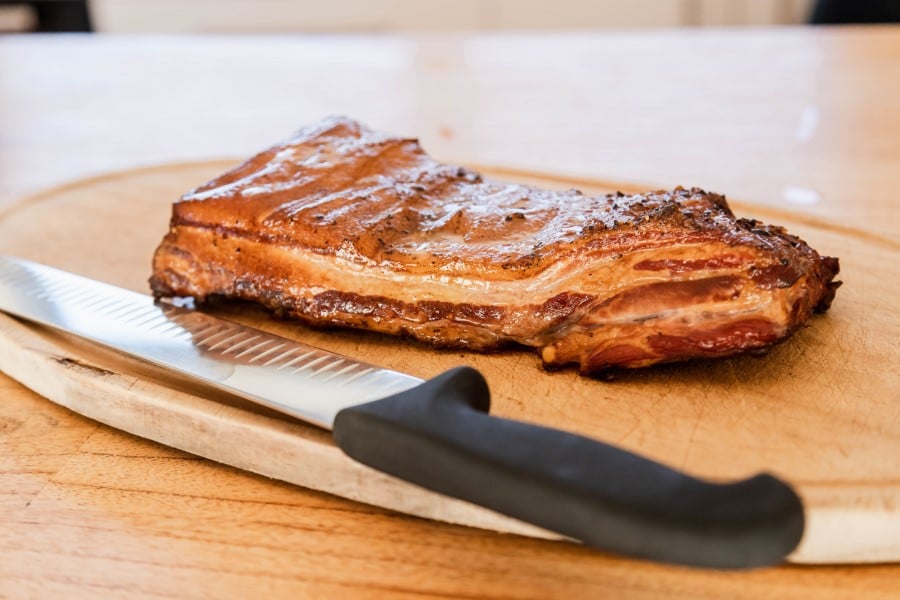 A succulent grilled pork belly on a wooden cutting board, glistening with a perfectly crispy layer, ready to be sliced and enjoyed.