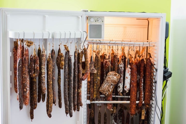 A variety of cured sausages hanging inside a modified refrigerator, being used as a drying and curing chamber.