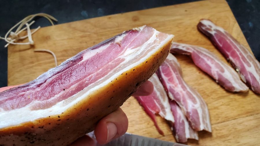 Picture of cold smoked dry cured bacon from the side, with the skin still on the bacon.