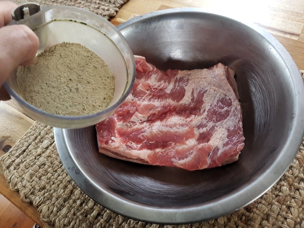 Adding salt cure to meat inside a bowl for making dry cured meat.