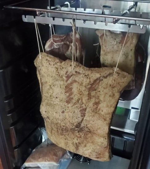 Cured pork belly hanging inside a drying fridge.