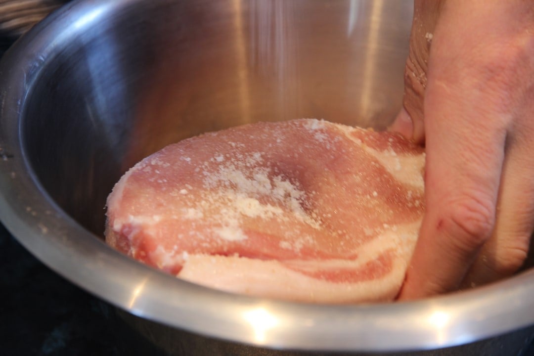 Pork meat with a sale cure in a bowl. With a hand to mix the cure.