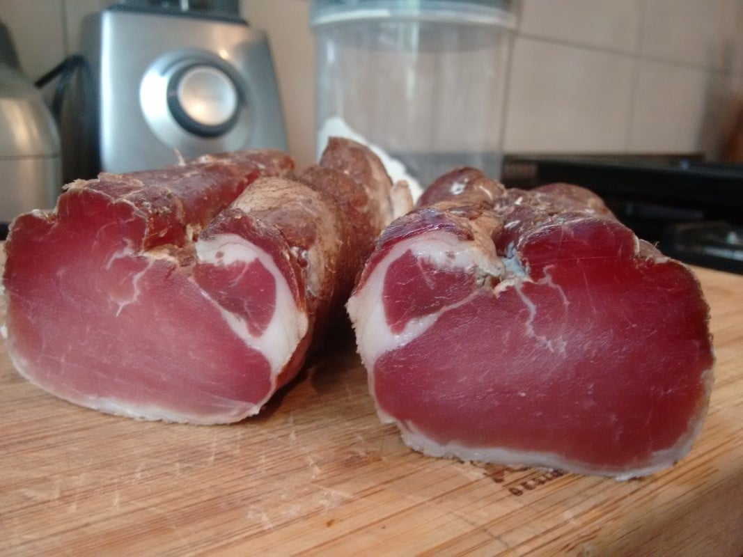 Dry cured lonza meat cut in half on a board.